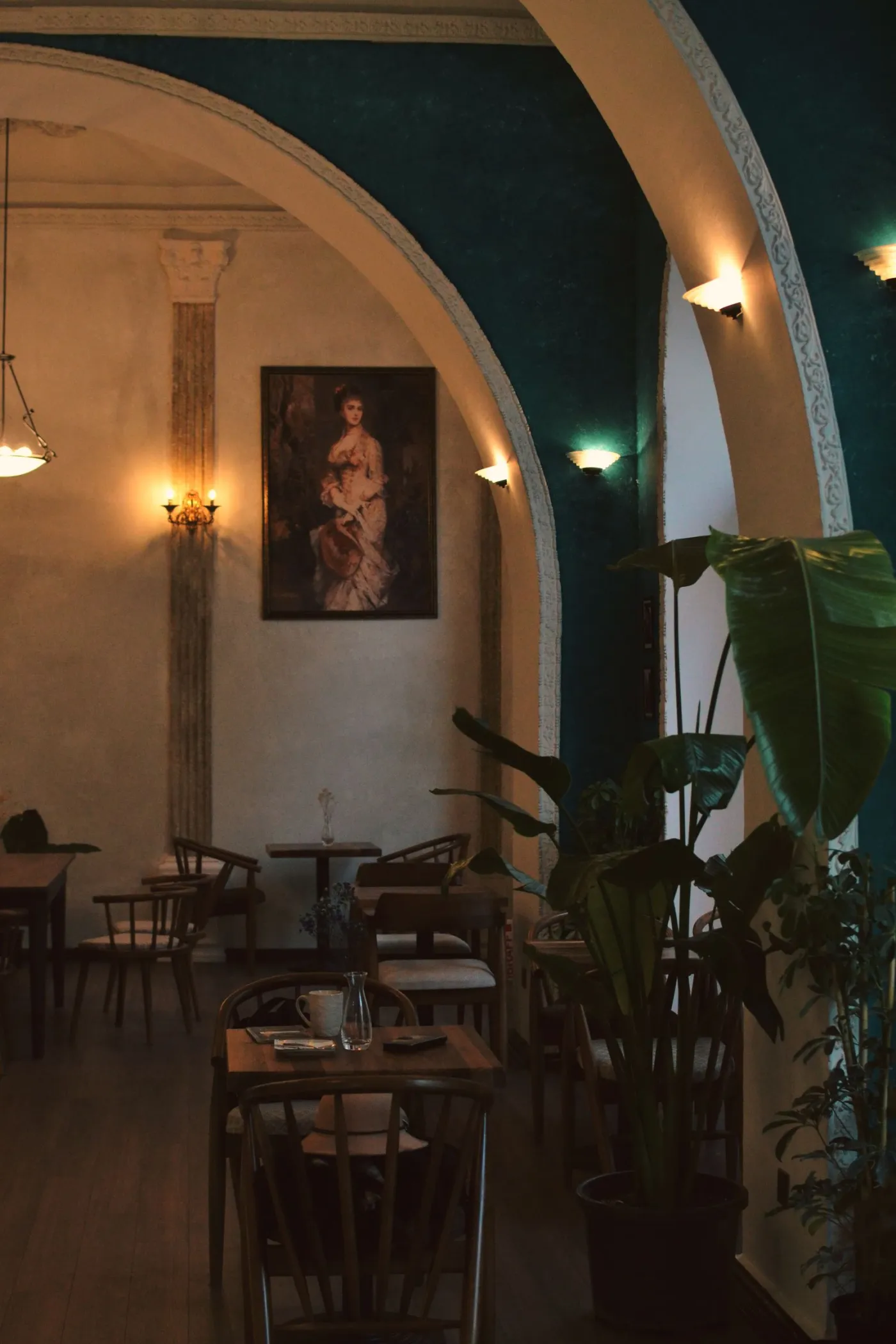 Arched dining room with a framed portrait and hanging plants.
