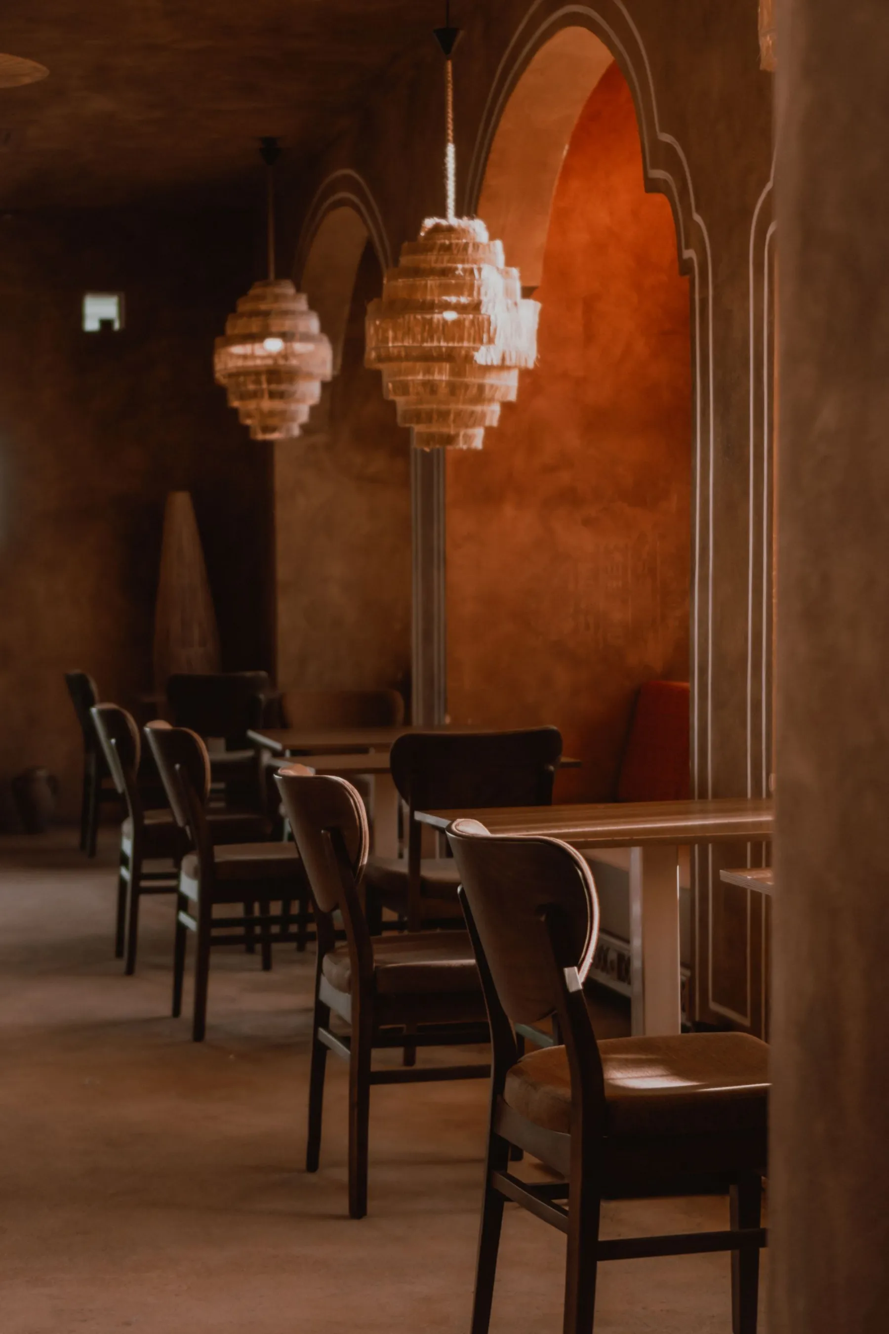 Warm-toned arched dining room with woven pendant lights and dark timber chairs.
