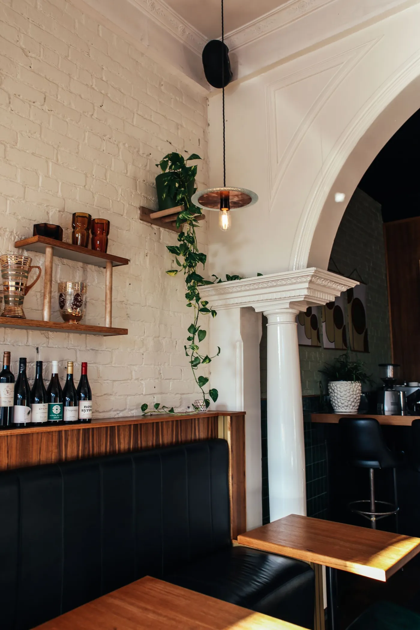 Bar corner with a brick wall, open wine shelving and a dark leather banquette.
