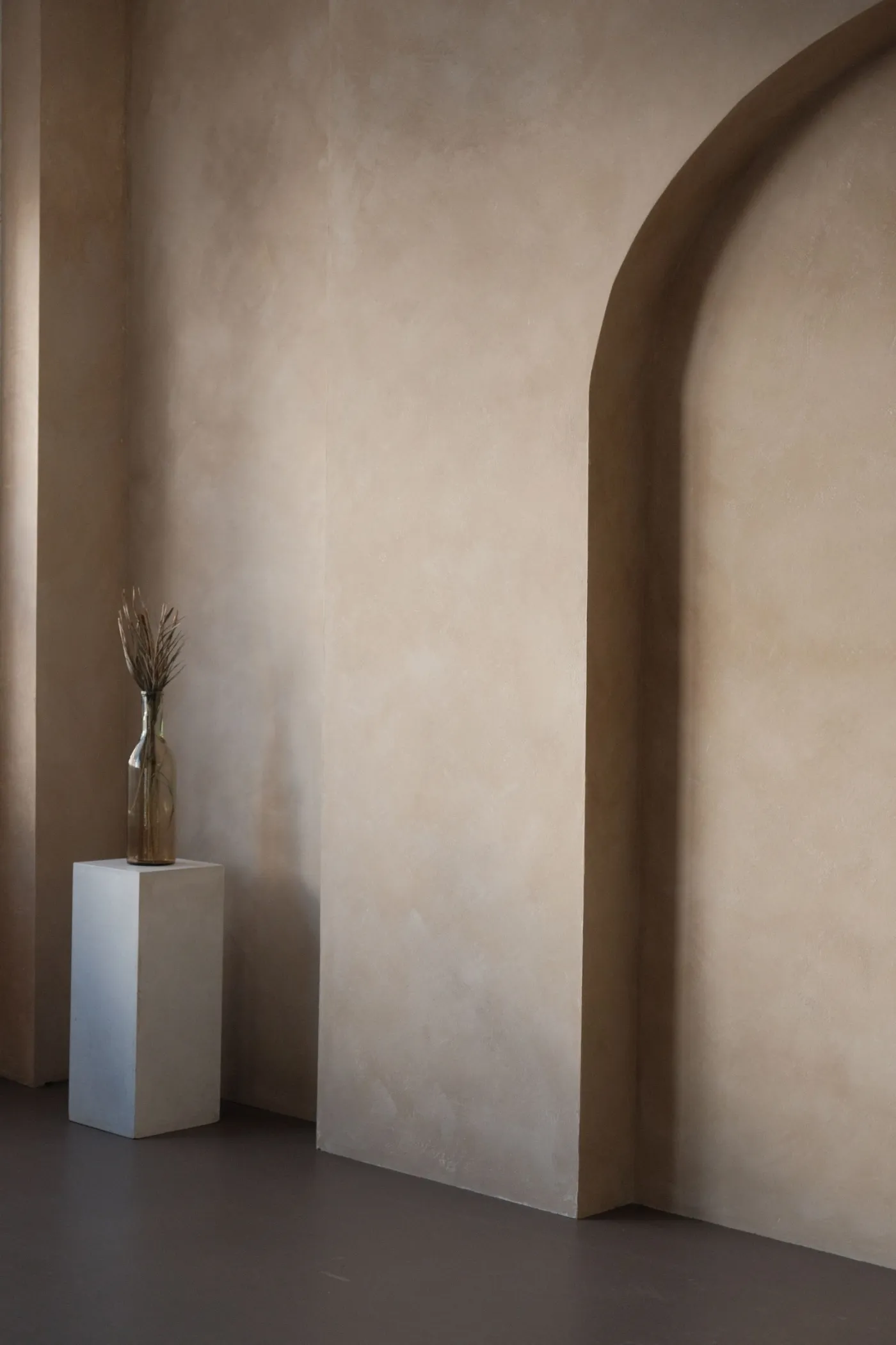 Warm plaster wall with an arched niche and a small pedestal.