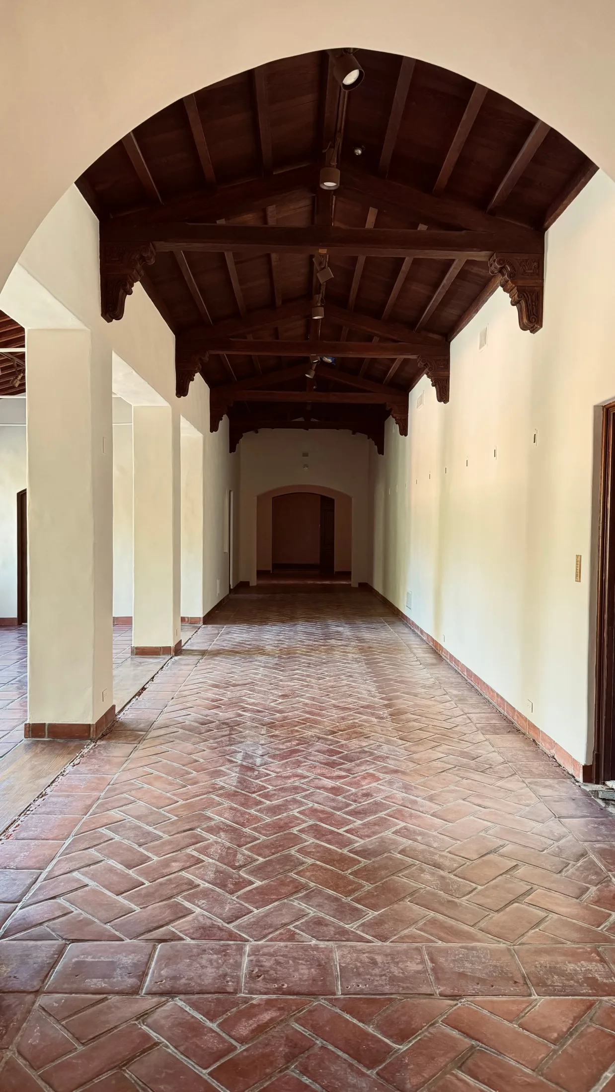 Beamed corridor with carved wood ceiling brackets and terracotta flooring.
