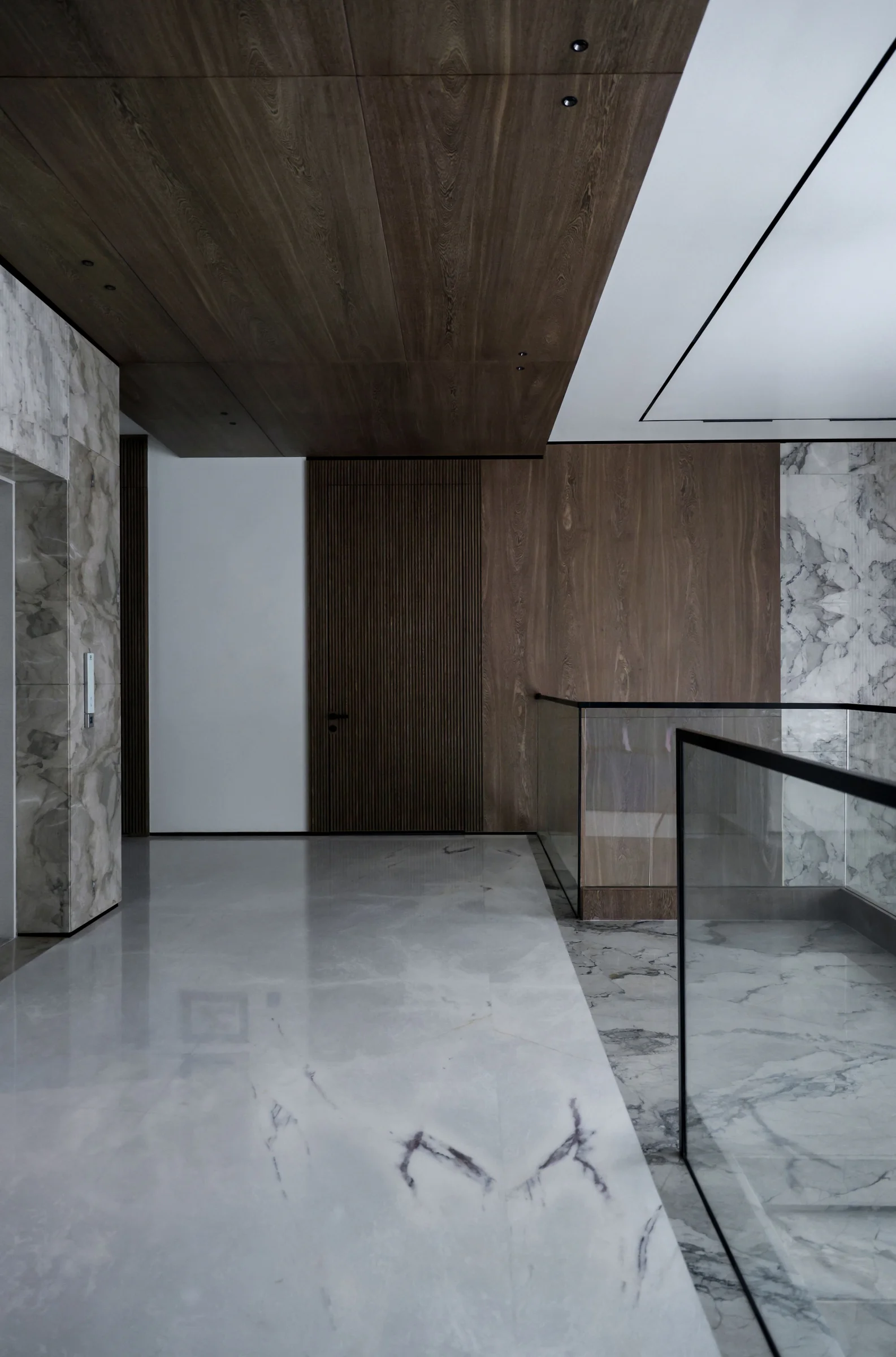 Stairwell landing with walnut wood paneling, stone flooring and a glass balustrade.